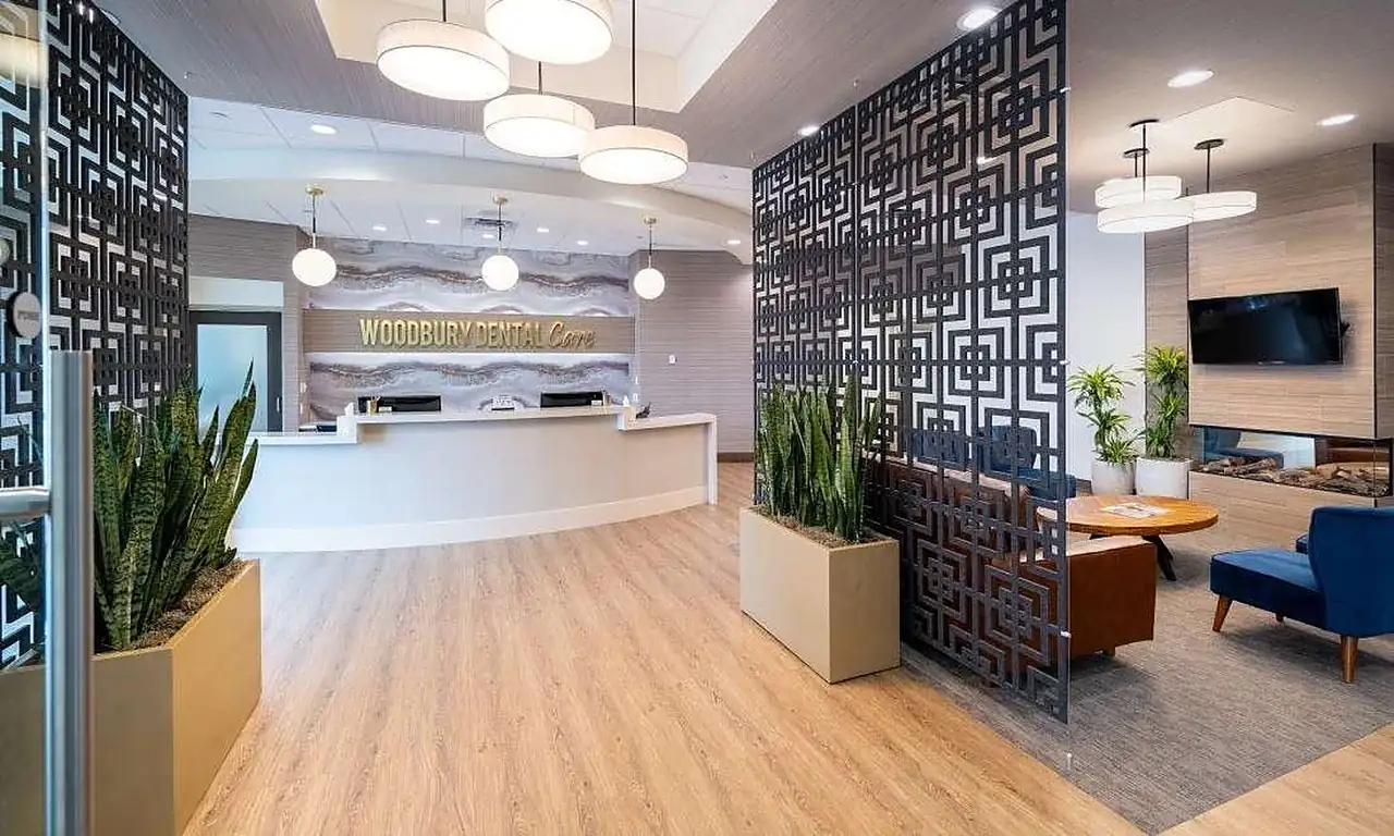 The lobby at Woodbury Dental Care: the reception desk with the practice's name in gold lettering, a patterned screen, and the fireside lounge beside it.