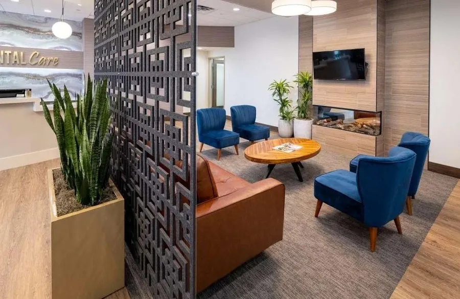 The lounge at Woodbury Dental Care: blue armchairs and a round table in front of a fireplace and TV.